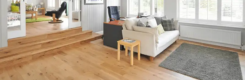 A modern living room with professionally installed laminate flooring, a beige sofa, a small side table, a gray rug, and large windows with white shutters in Cape Coral, FL